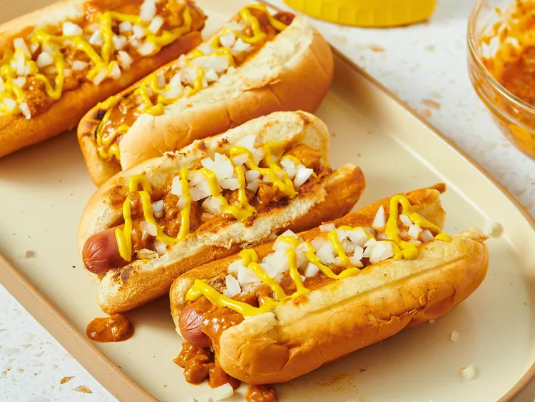 Delicious Detroit-style hotdogs sit atop golden buns topped with Coney chili sauce, chopped white onion, and yellow mustard.