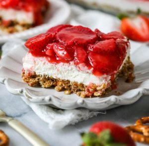 Strawberry Pretzel Salad depicting red juicy strawberries sitting atop white whipped cream cheese frosting, and crunchy brown pretzels
