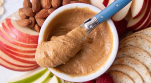 Woodstock nut butter in a white bowl, surrounded by sliced apples.